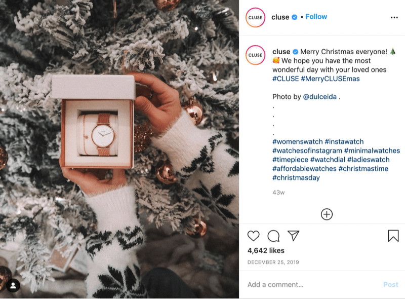 instagram ziņa no @cluse, kurā parādīts attēls ar sniegpārsliņu džemperi, kurš @dulceida tur pulksteni sniegota koka priekšā ar mirkļbirku #cluse un #meryclusemas